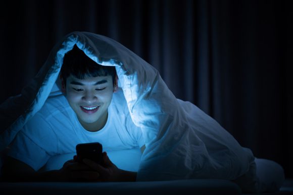잠자리에서 스마트폰을 보고 있는 젊은 남성